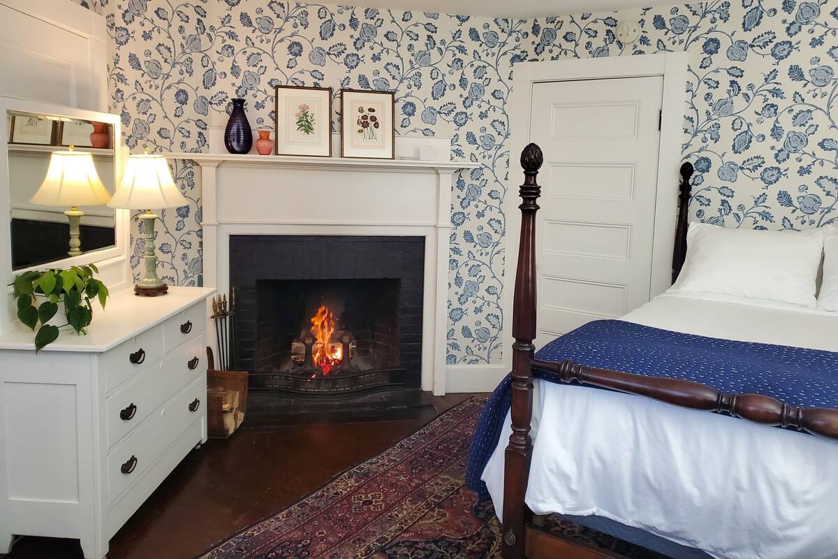 Un dormitorio con chimenea, cama, cómoda y espejo.