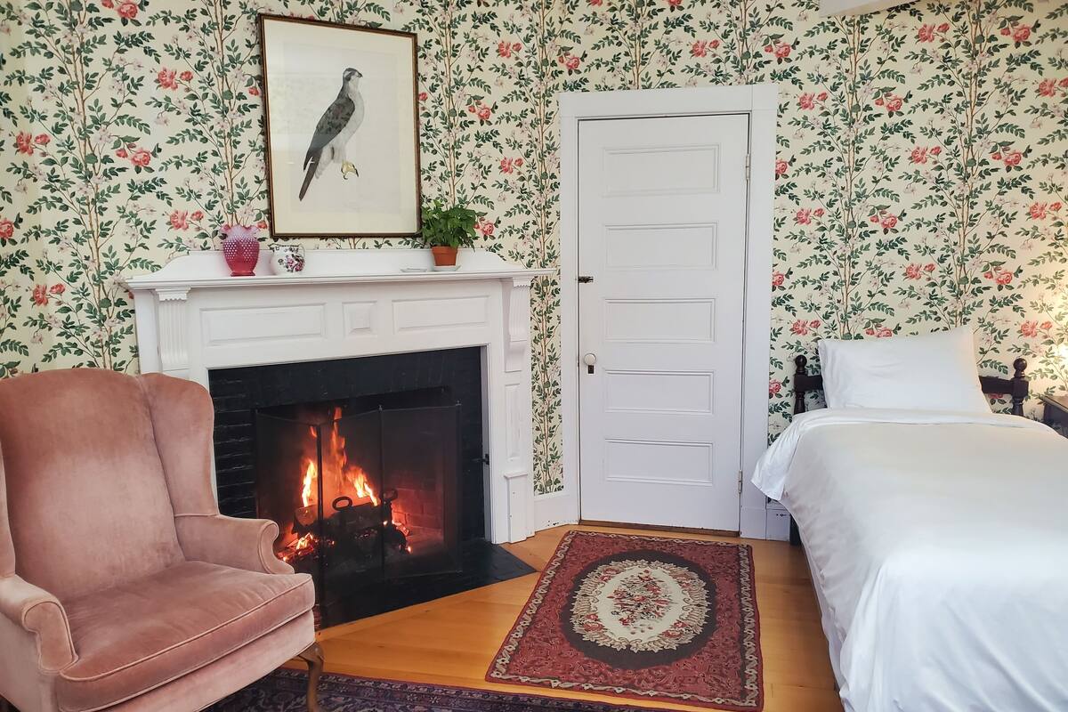 Una habitación con chimenea, cama, sillón y papel tapiz floral.