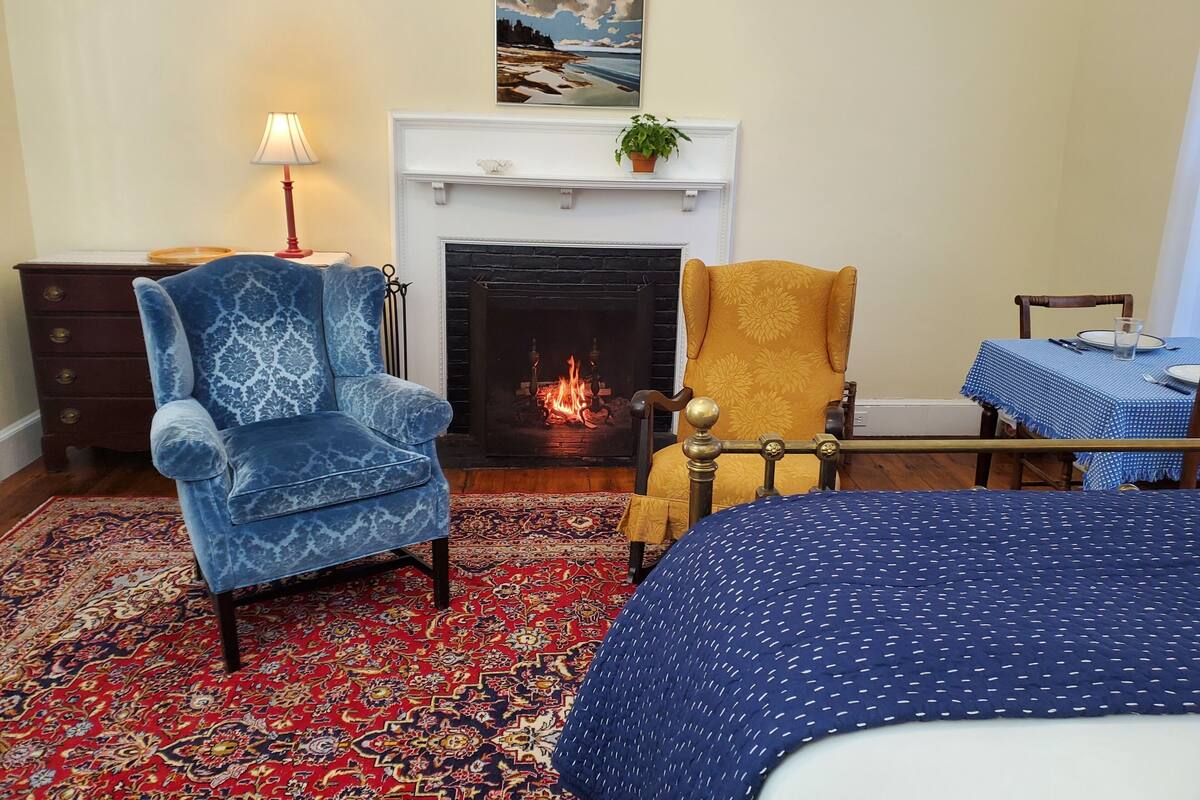 Una habitación con chimenea, dos sillones, una mesa con mantel azul y alfombra estampada.