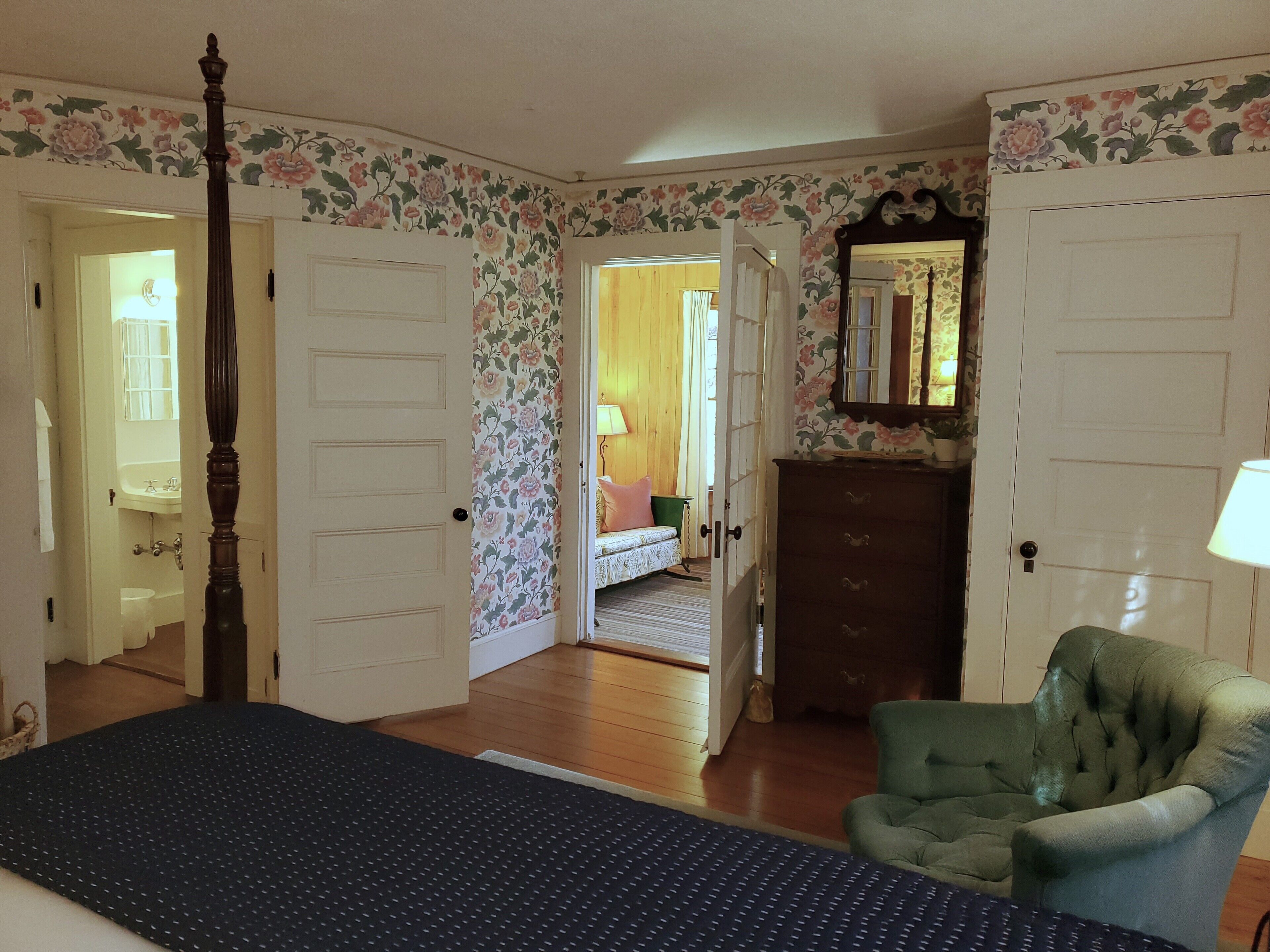A bedroom with a bed, a green armchair, a dresser, and a mirror.