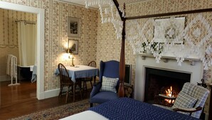 A traditional room with a bed, a fireplace, a table with chairs, and a shower area.
