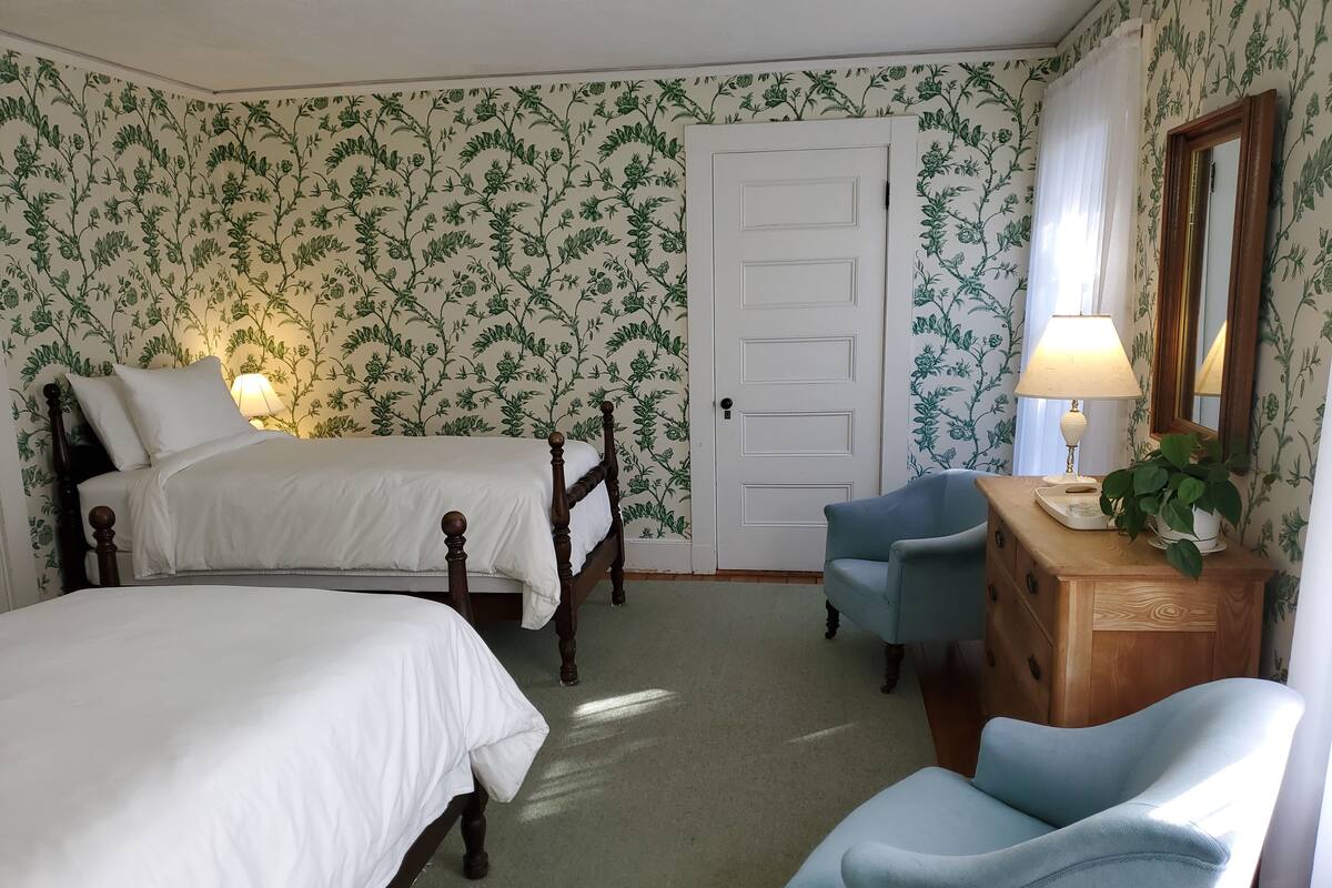 Un dormitorio con dos camas, un aparador, una silla y un espejo.