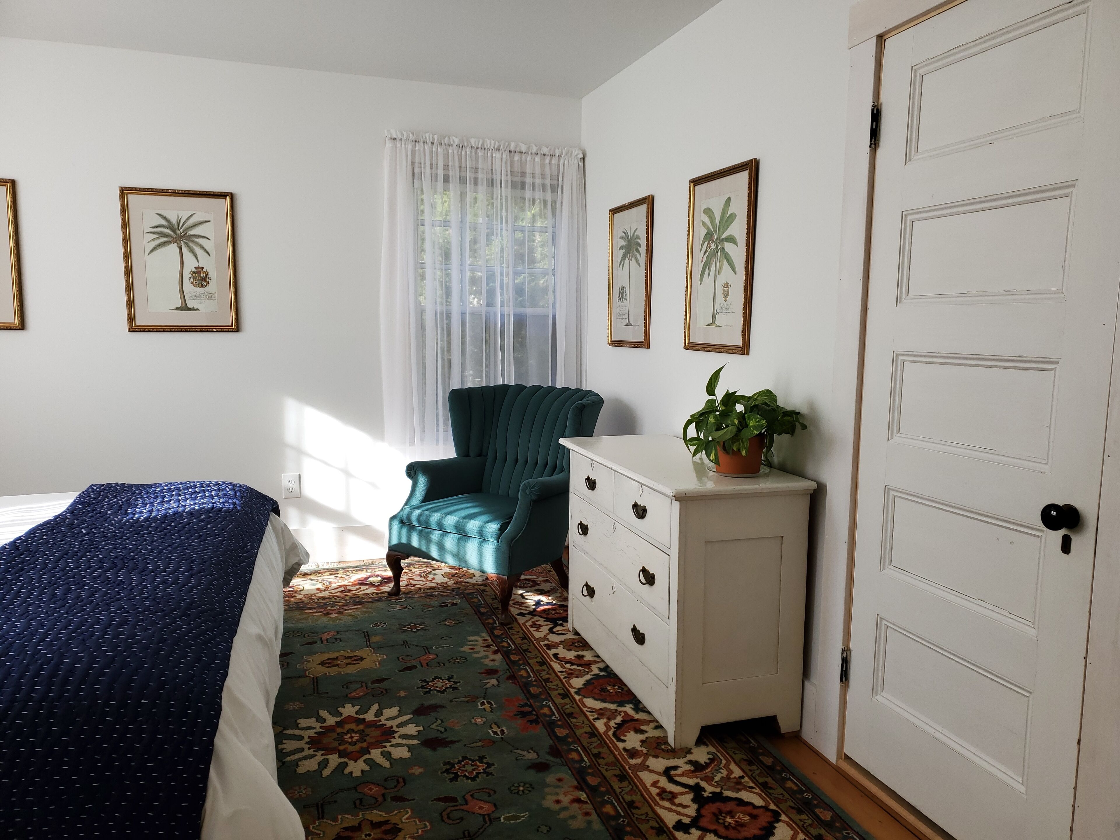 Un dormitorio con cama, una silla, cómoda y una puerta.