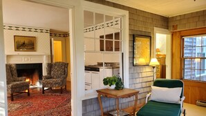 A cozy living room with a fireplace, two armchairs, a dining table, and a green lounge chair. - Harbourside Inn (Northeast Harbor)