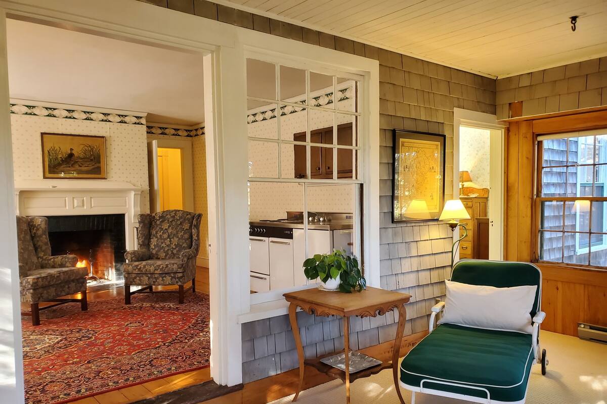 Un salón acogedor con chimenea, dos sillones, una mesa de comedor y un sillón reclinable verde.