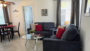 A modern living room with a dark grey sofa, red cushions, a glass coffee table with a plant, and a dining area with a black table and chairs. - C2 Perfect location in historic city center, near beaches, patio, free parking! (St. Augustine)