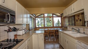 A kitchen with a stove, microwave, and sink. There is a dining table with chairs and a window with blinds. - Coates by Hauserman Rentals (Tahoe City)