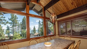 A wooden dining table with chairs, large windows, and a hanging light fixture. - Coates by Hauserman Rentals (Tahoe City)
