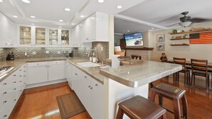 Una cocina moderna con armarios blancos, una isla grande y una zona de comedor con sillas de madera y una barra.