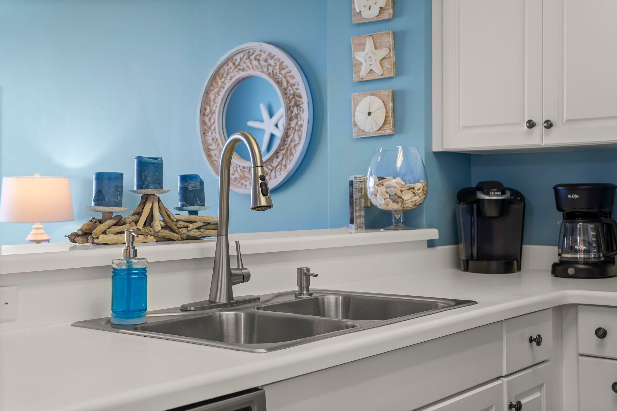 A kitchen with a double sink, a blue wall, and nautical-themed decorations.