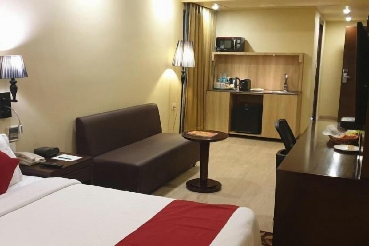 A hotel room with a bed, a sofa, a small table, a desk, and a kitchenette.