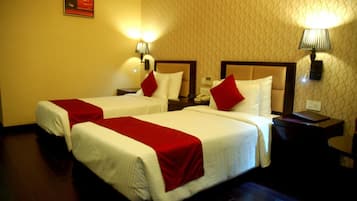 A hotel room with two beds, each with a red and white bedspread, and a nightstand with a lamp between them.