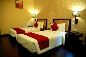 A hotel room with two beds, each with a red and white bedspread, and a nightstand with a lamp between them.