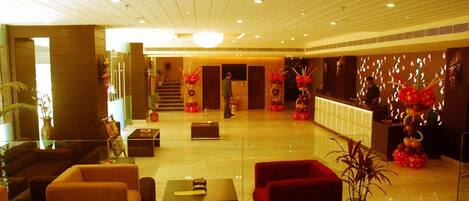 A hotel lobby with a reception desk, seating area, and a staircase leading to an upper floor.