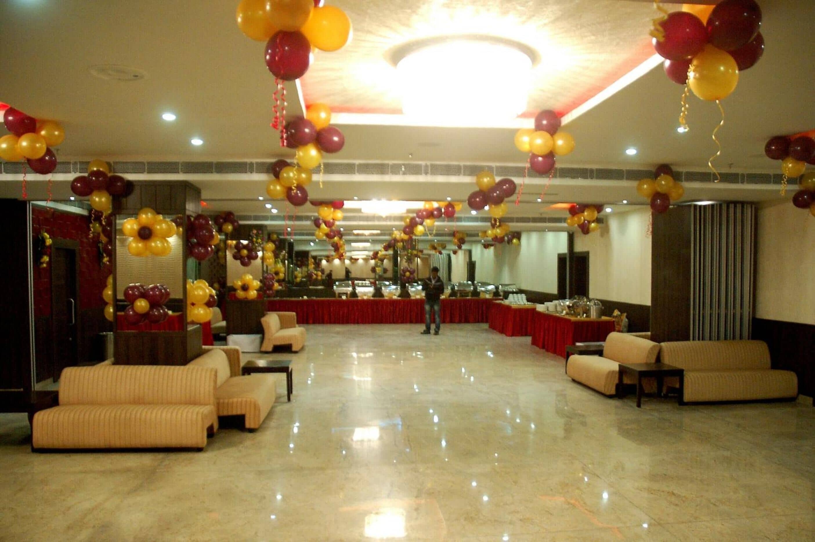 A spacious hall with a polished marble floor, red and gold balloons, and a buffet setup.