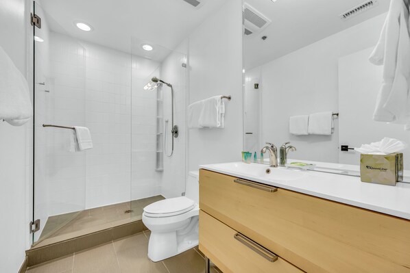 Un baño moderno con cabina de ducha de vidrio, inodoro blanco y tocador con espejo.