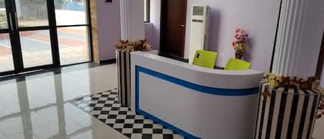 Una taquilla de recepció amb un sòl a escac i llit, una finestra que mostra el paisatge exterior, i un aire condicionat fixat a la paret.