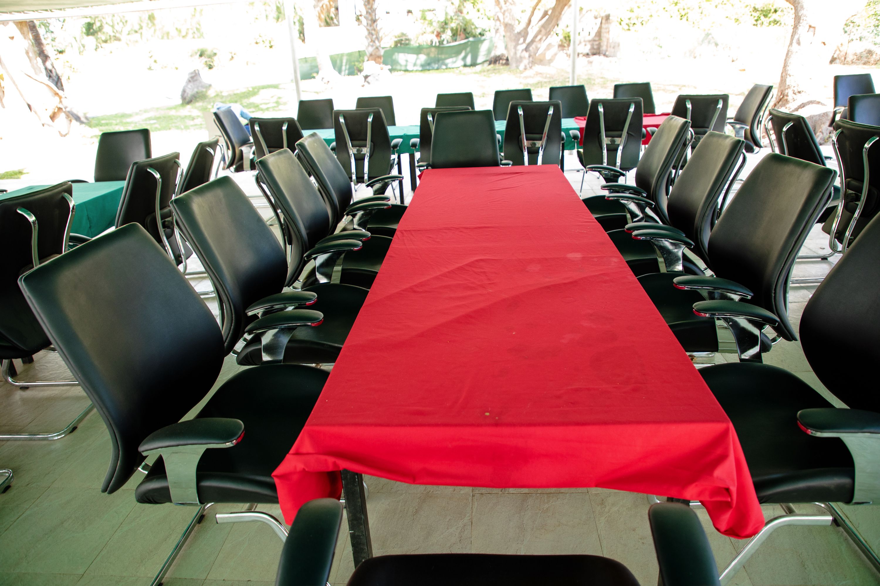 A conference room with a long table covered by a red tablecloth, surrounded by black chairs.