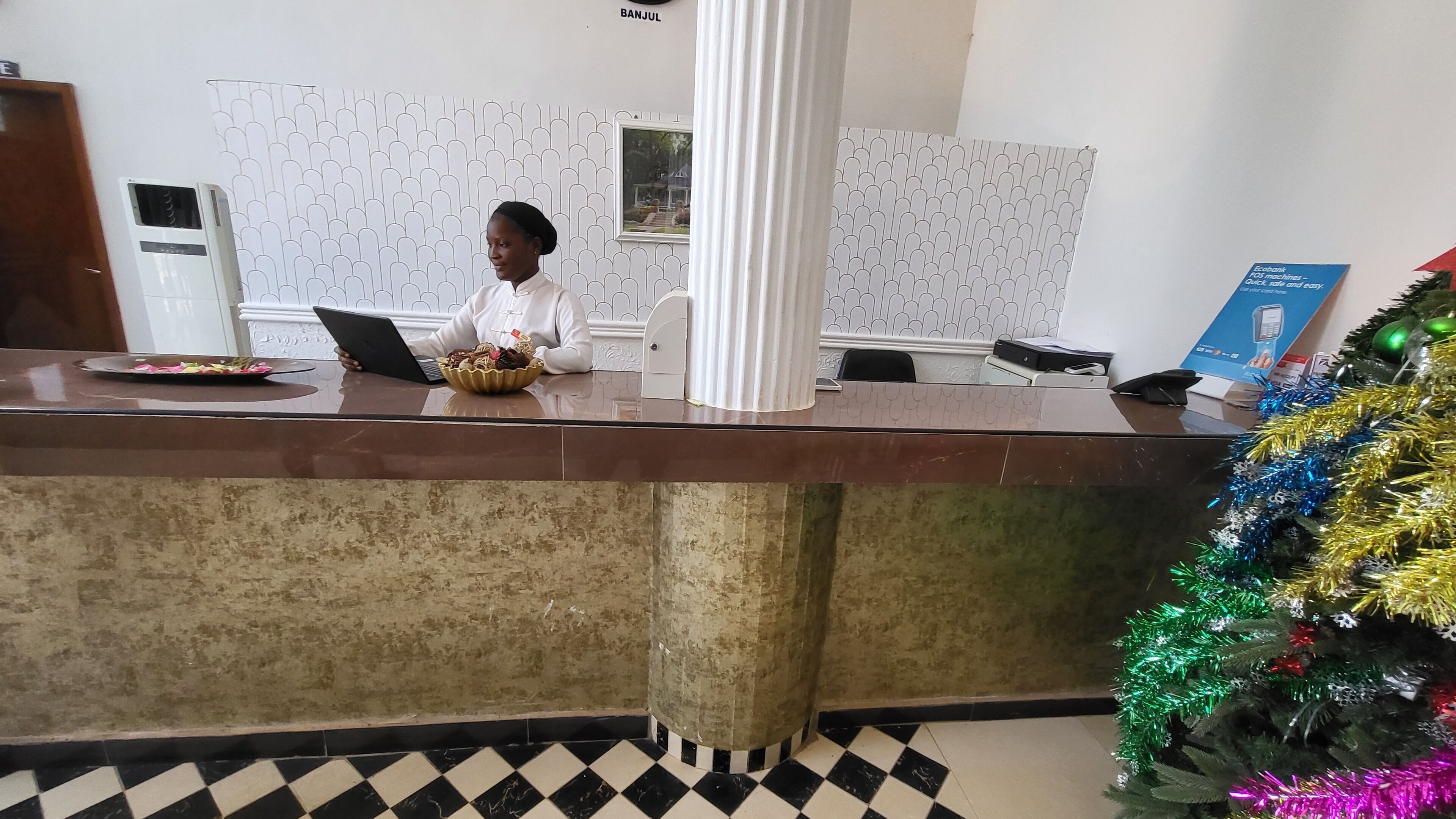 A reception area with a counter, a laptop, a decorative bowl, a wall-mounted air conditioner, and a Christmas tree.