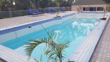 Una piscina con bordes de azulejos azules y blancos, rodeada de sillas de descanso y una terraza con baldosas.
