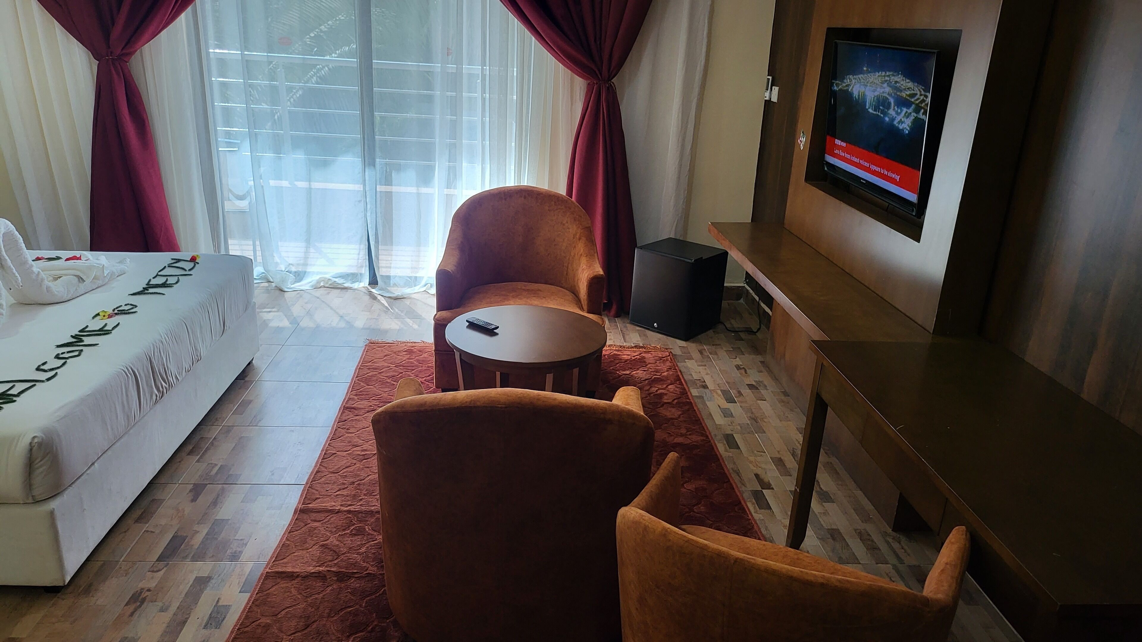 A hotel room with a bed, two armchairs, a small round table, a TV, and a window with curtains.