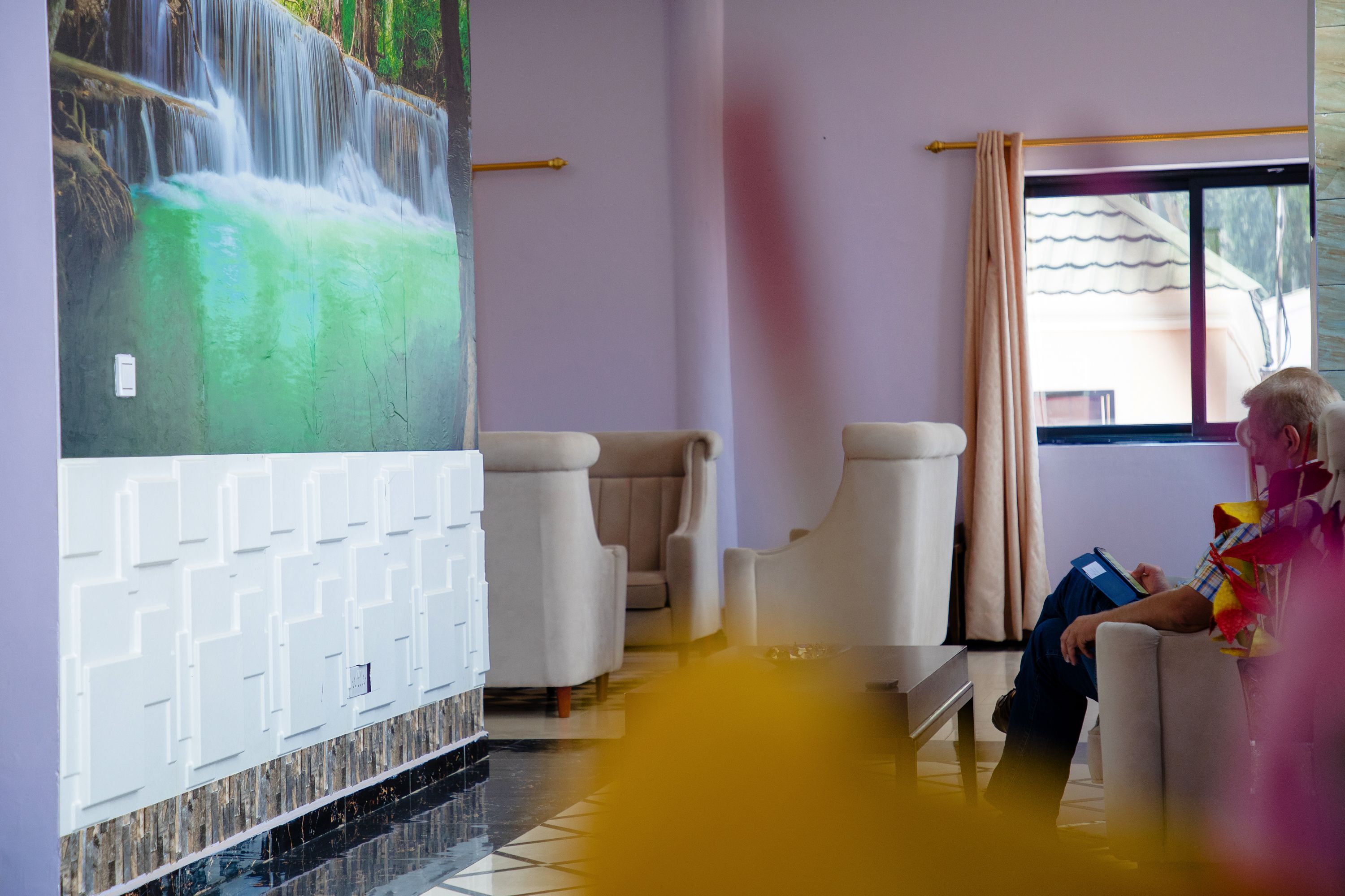 A room with a mural of a waterfall, a window with a view, and a seating area with a person reading.