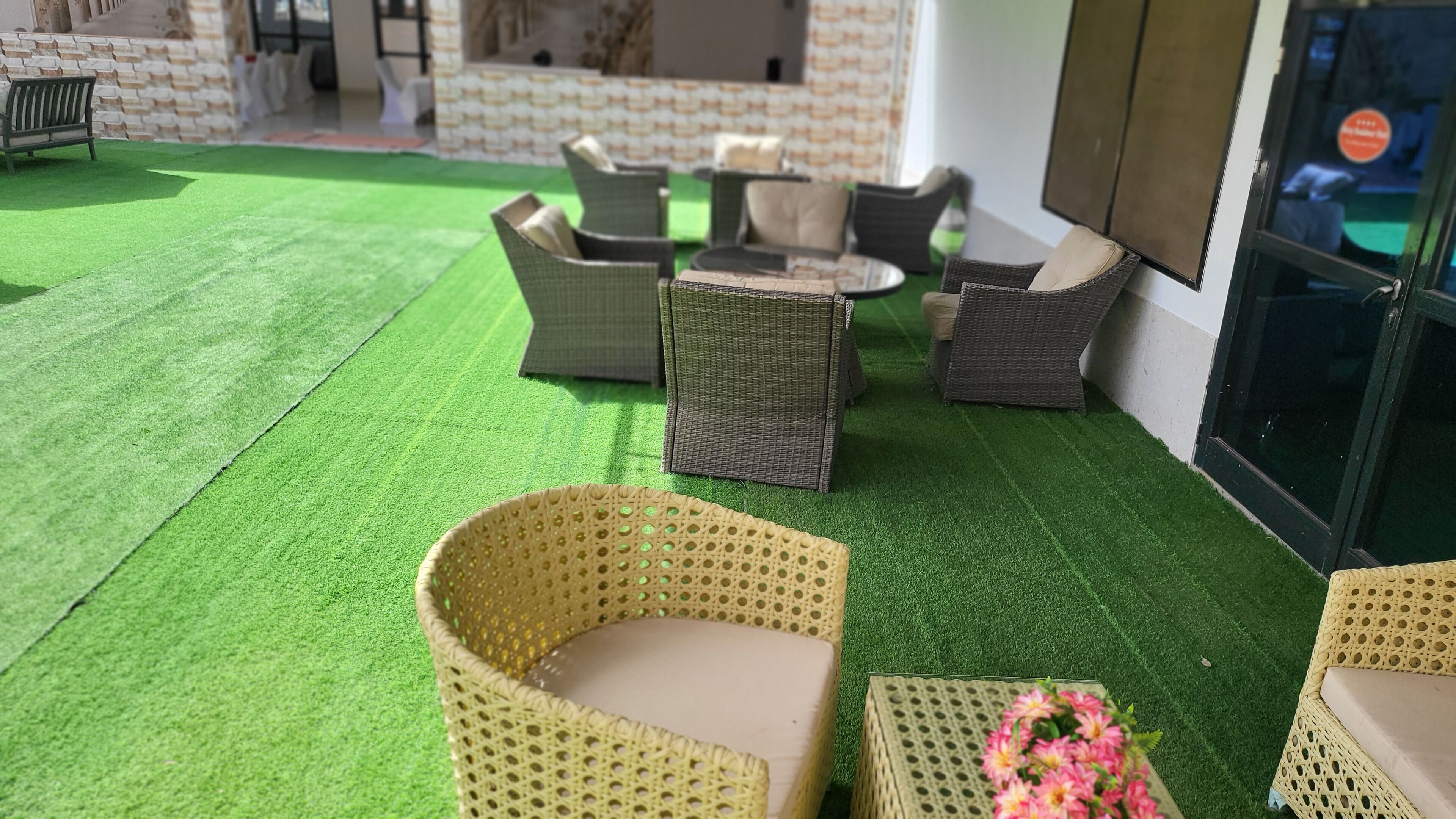 An outdoor seating area with wicker furniture on artificial grass, near a building with a patterned facade.