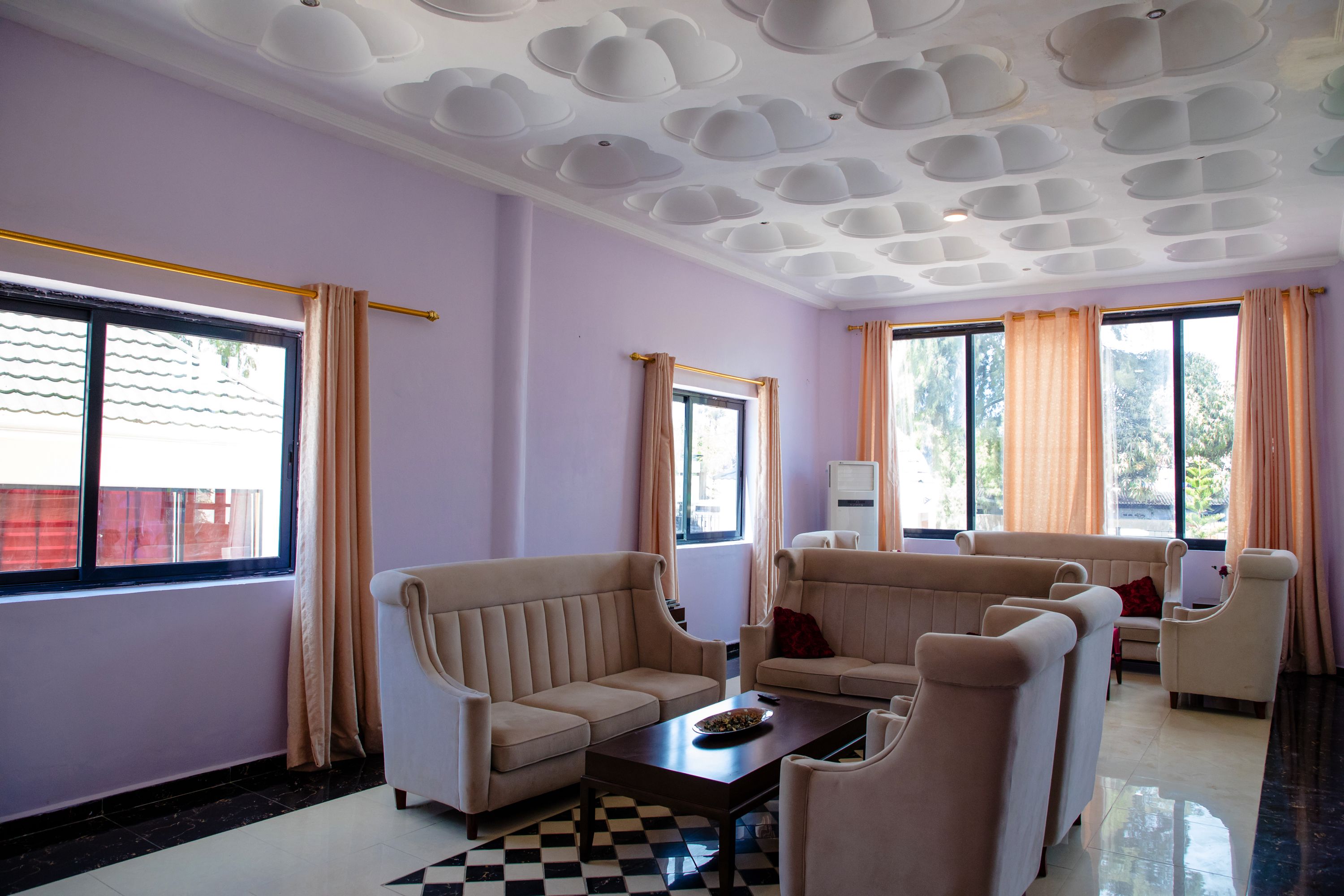 A living room with a checkered floor, beige sofas, a coffee table, and a ceiling with a unique design.