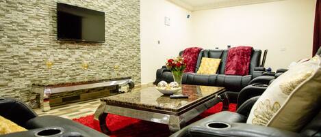 A modern living room with a stone wall, a flat-screen TV, a red carpet, and leather furniture.