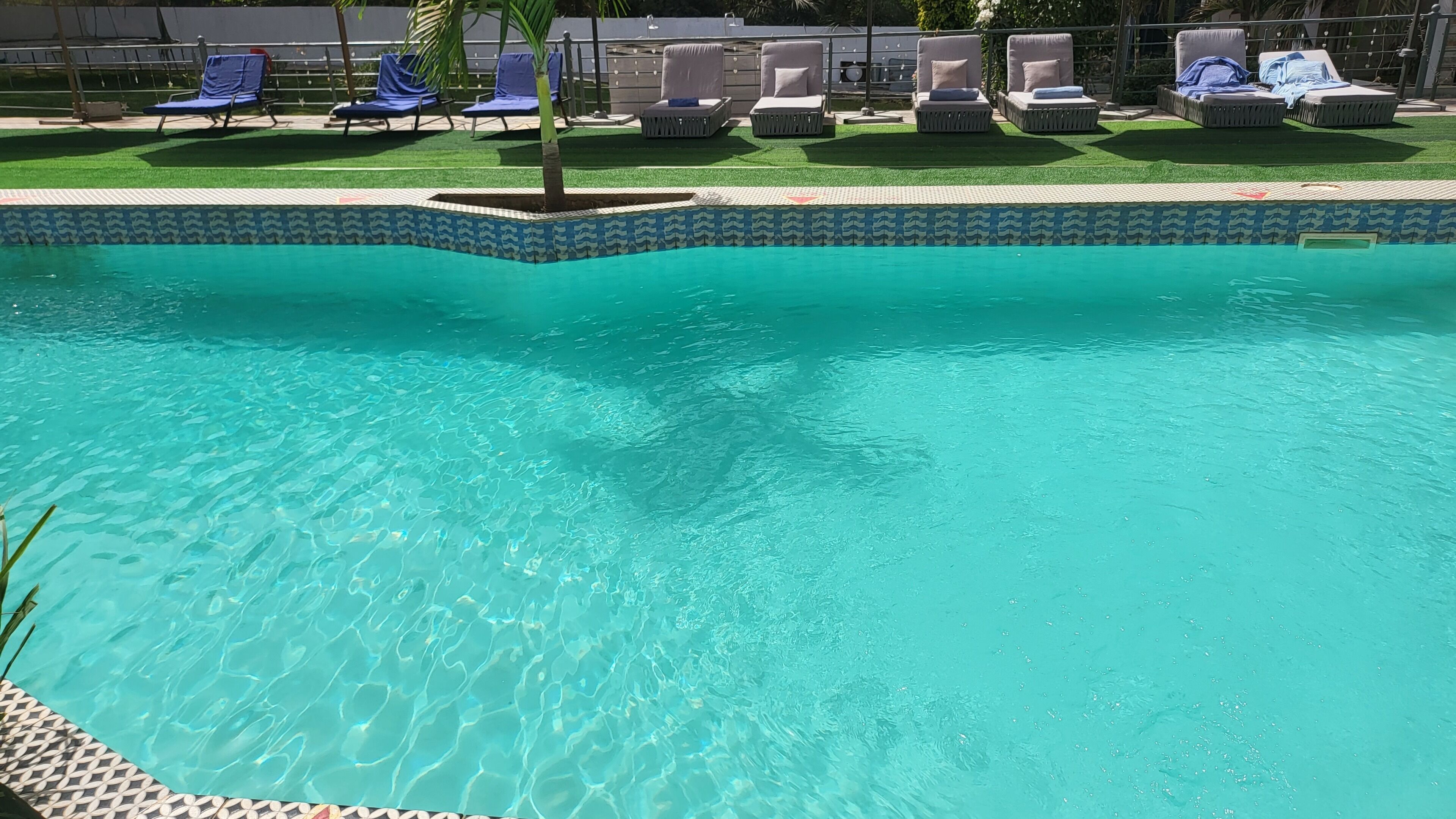 A swimming pool with clear blue water, surrounded by lounge chairs and a tiled deck.