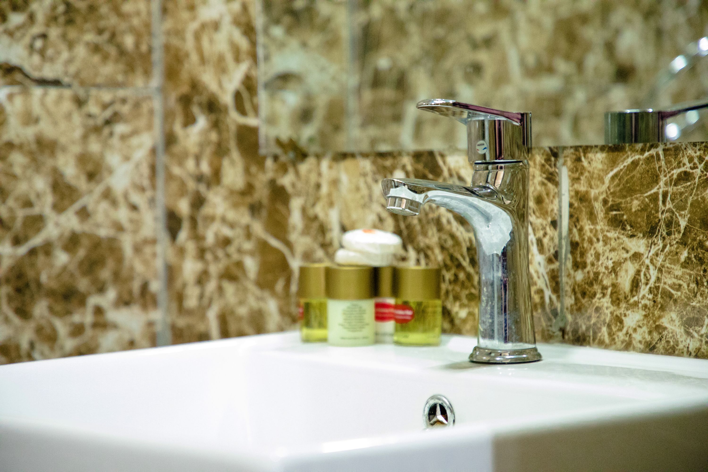 A bathroom sink with a chrome faucet, a marble backsplash, and three bottles of toiletries on the counter.