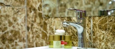 Un lavabo de salle de bain avec un robinet chromé, un pare-éclaboussures en marbre et trois flacons de produits de toilette posés sur le comptoir.