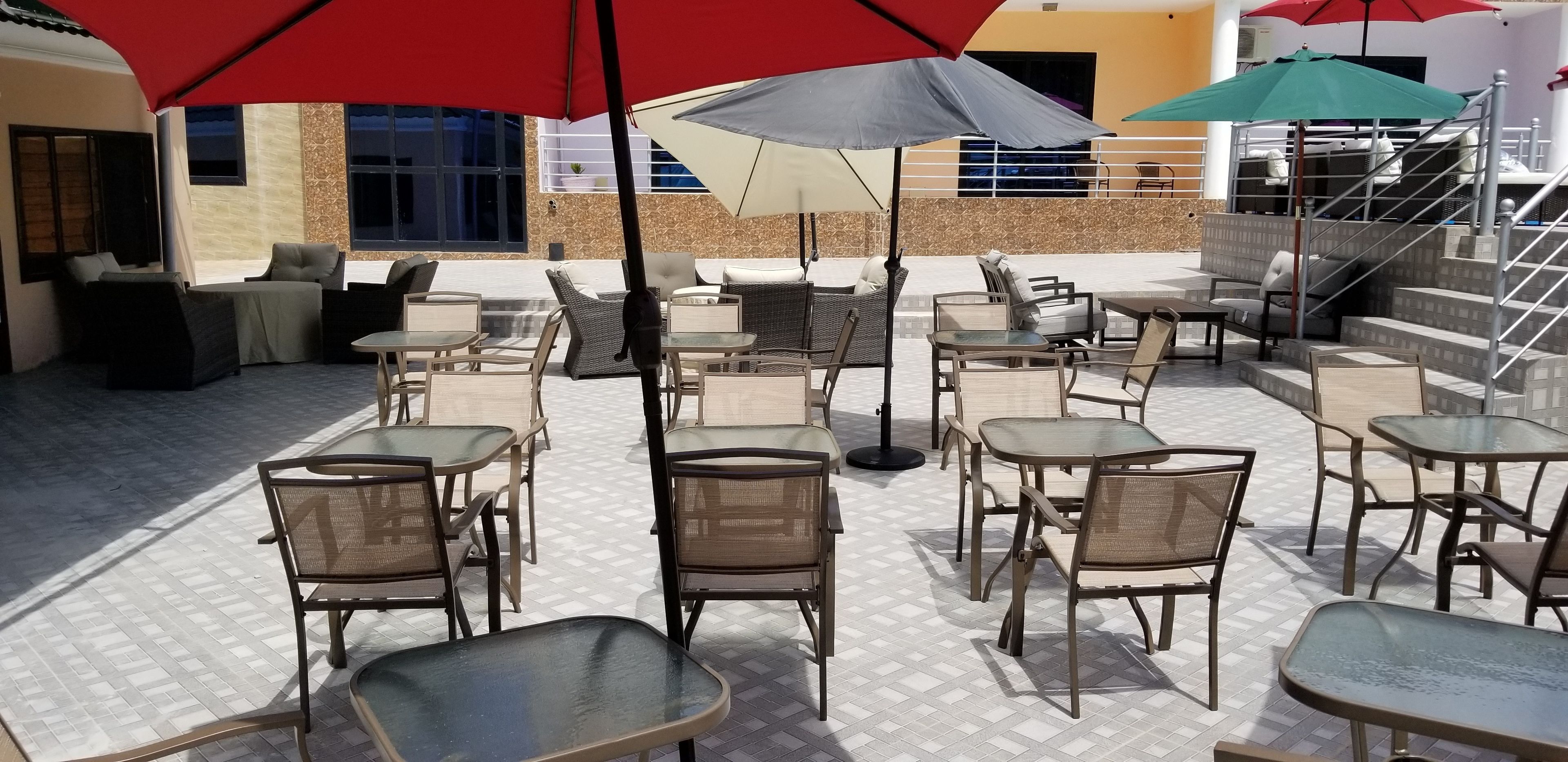 An outdoor patio with multiple tables and chairs, some under umbrellas, and a staircase leading to an upper level.