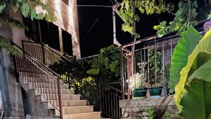 A stone staircase leading to a building with a metal railing, surrounded by lush greenery and flowering plants. - Denis Guest House (Gjirokastër)