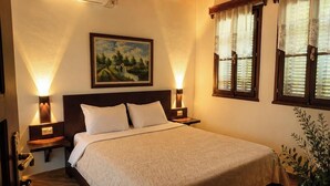 A bedroom with a bed, two bedside lamps, a painting, and a ceiling light fixture. - Denis Guest House (Gjirokastër)