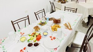 A dining area with a long table set for a meal, surrounded by chairs. - Denis Guest House (Gjirokastër)