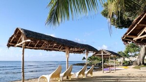 A beach with thatched-roof structures and white plastic chairs.