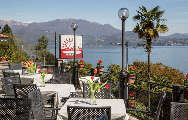 An outdoor seating area with tables and chairs, a sign for Hotel Sol, and a view of a lake with mountains in the background.