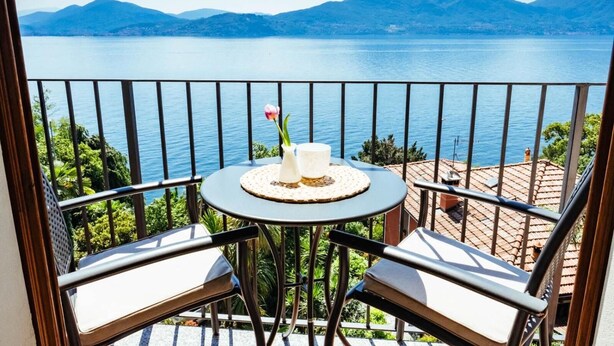 A balcony with a table and two chairs, overlooking a lake and mountains. - Albergo Sole (Cannero Riviera)
