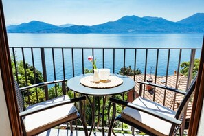 A balcony with a table and two chairs, overlooking a lake and mountains.
