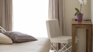 A bedroom with a bed, a chair, a small table with a potted orchid, and a window with curtains. - Albergo Sole (Cannero Riviera)