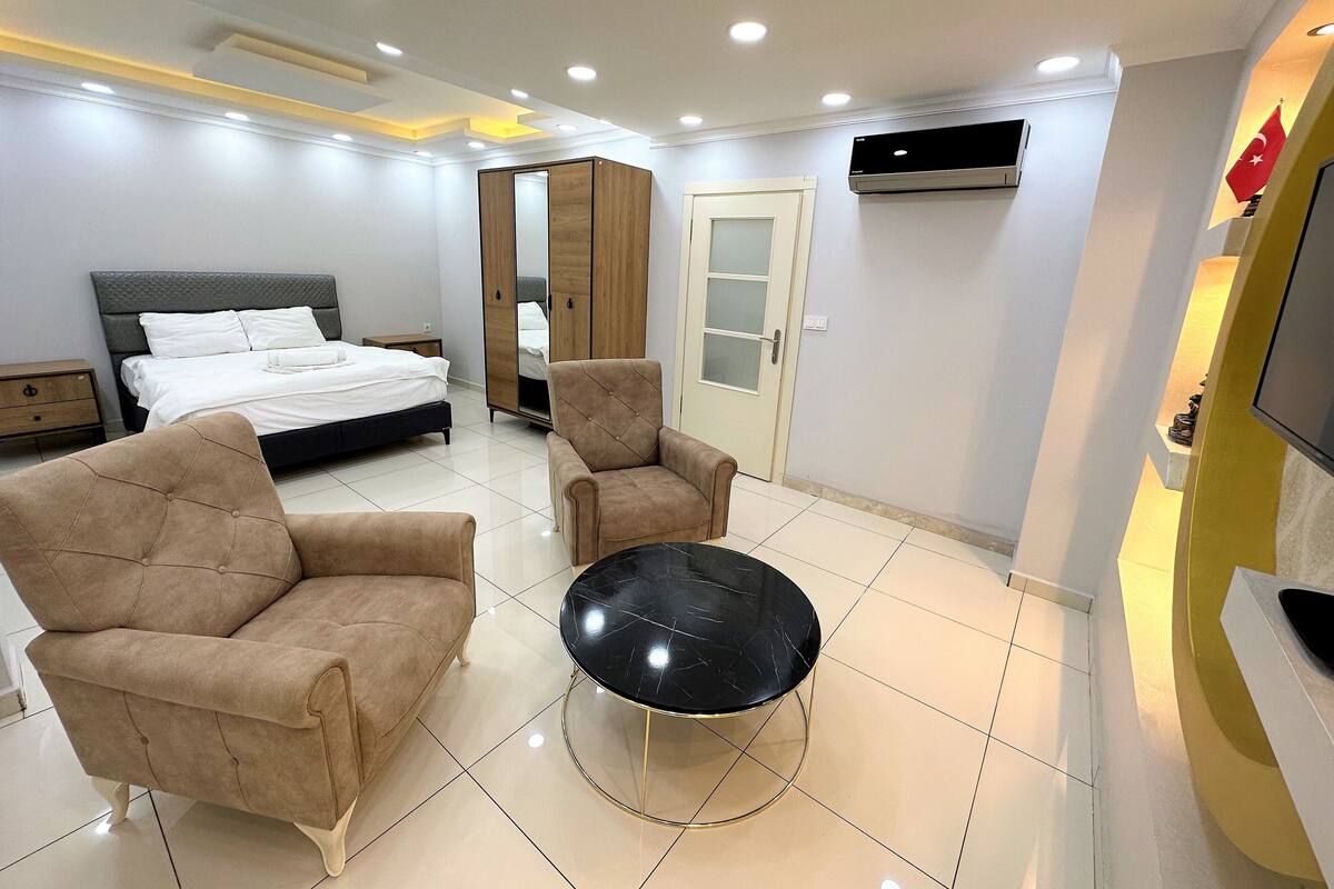 A modern bedroom with a bed, two armchairs, a round table, a wardrobe, and a TV.