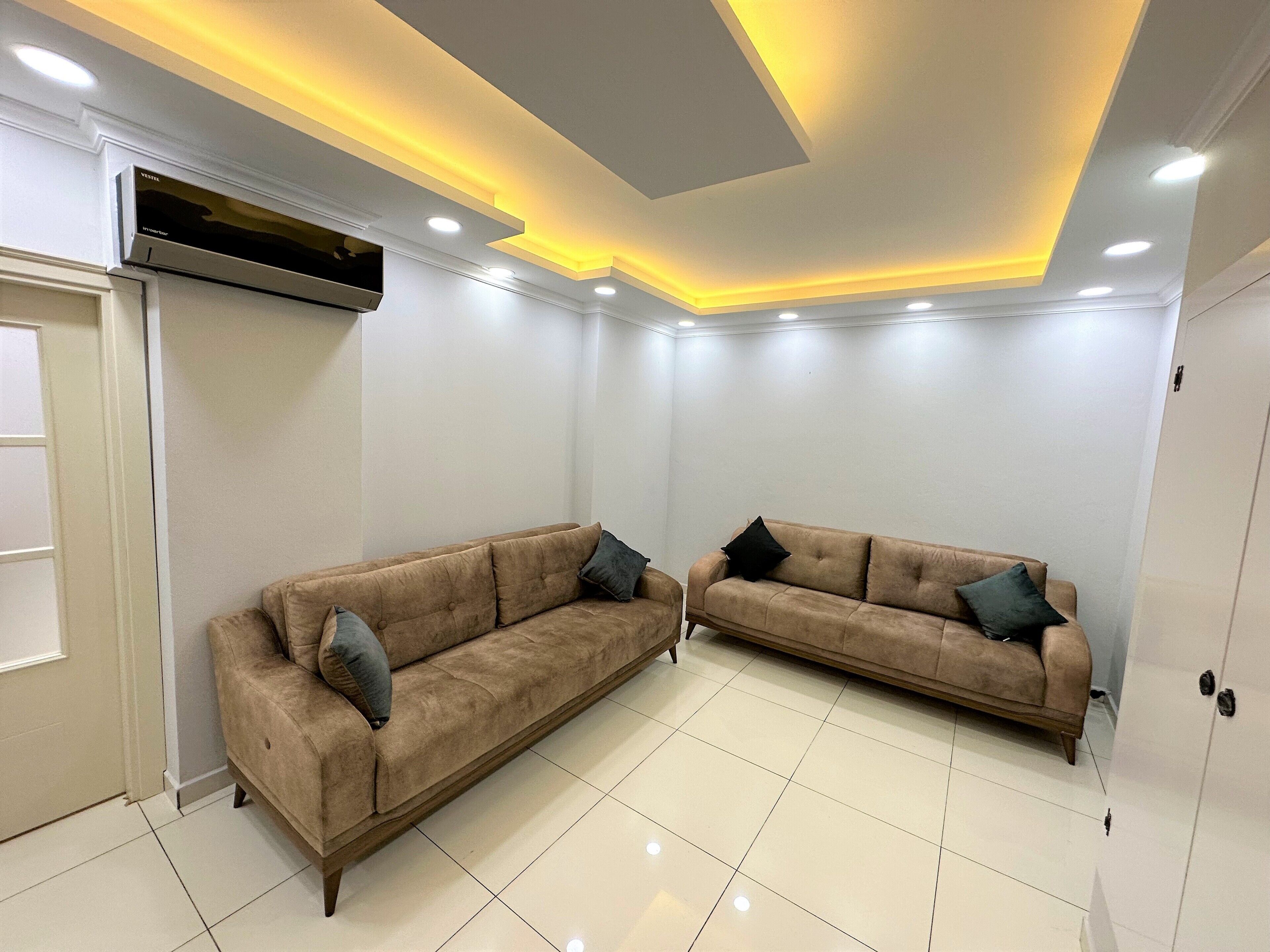A room with two sofas, a ceiling light fixture, and a wall-mounted air conditioning unit.