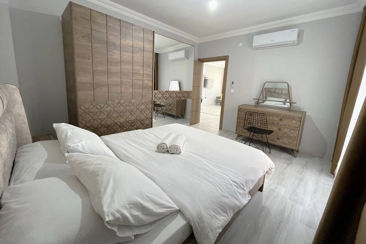 A modern hotel room with a large bed, a wooden wardrobe, a dresser, and a mirror.