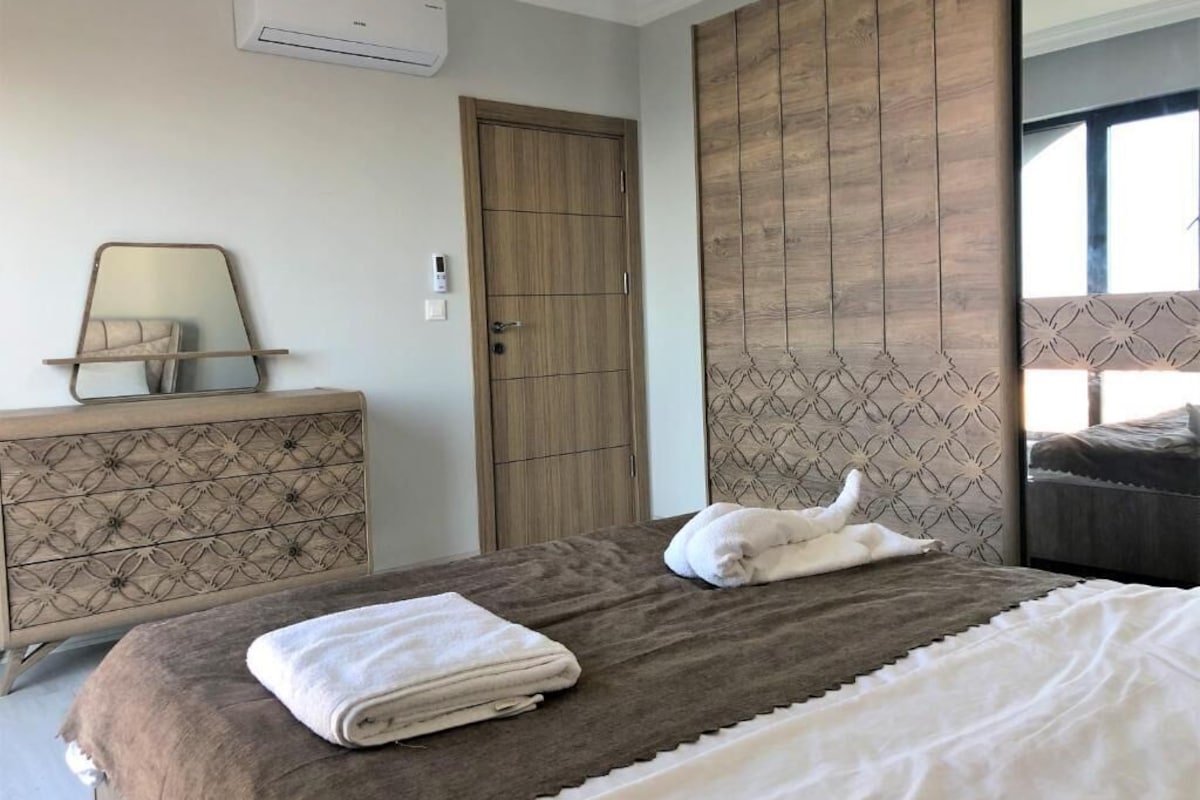 A bedroom with a bed, a dresser, an air conditioner, a door, and a patterned headboard.