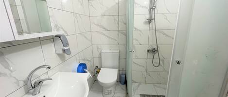 Un baño con lavamanos, inodoro y ducha envuelta en vidrio.