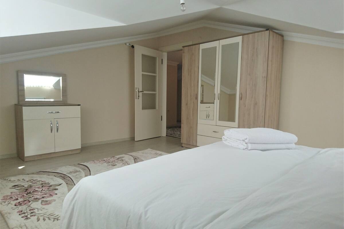 A bedroom with a bed, a wardrobe, a mirror, and a door leading to another room.