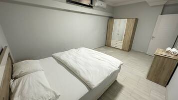 Quarto com uma cama, guarda-roupa e uma pequena prateleira com toalhas.