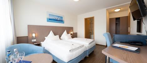 Een hotelkamer met twee bedden, een bureau, een stoel, een televisie en een schilderij aan de muur.
