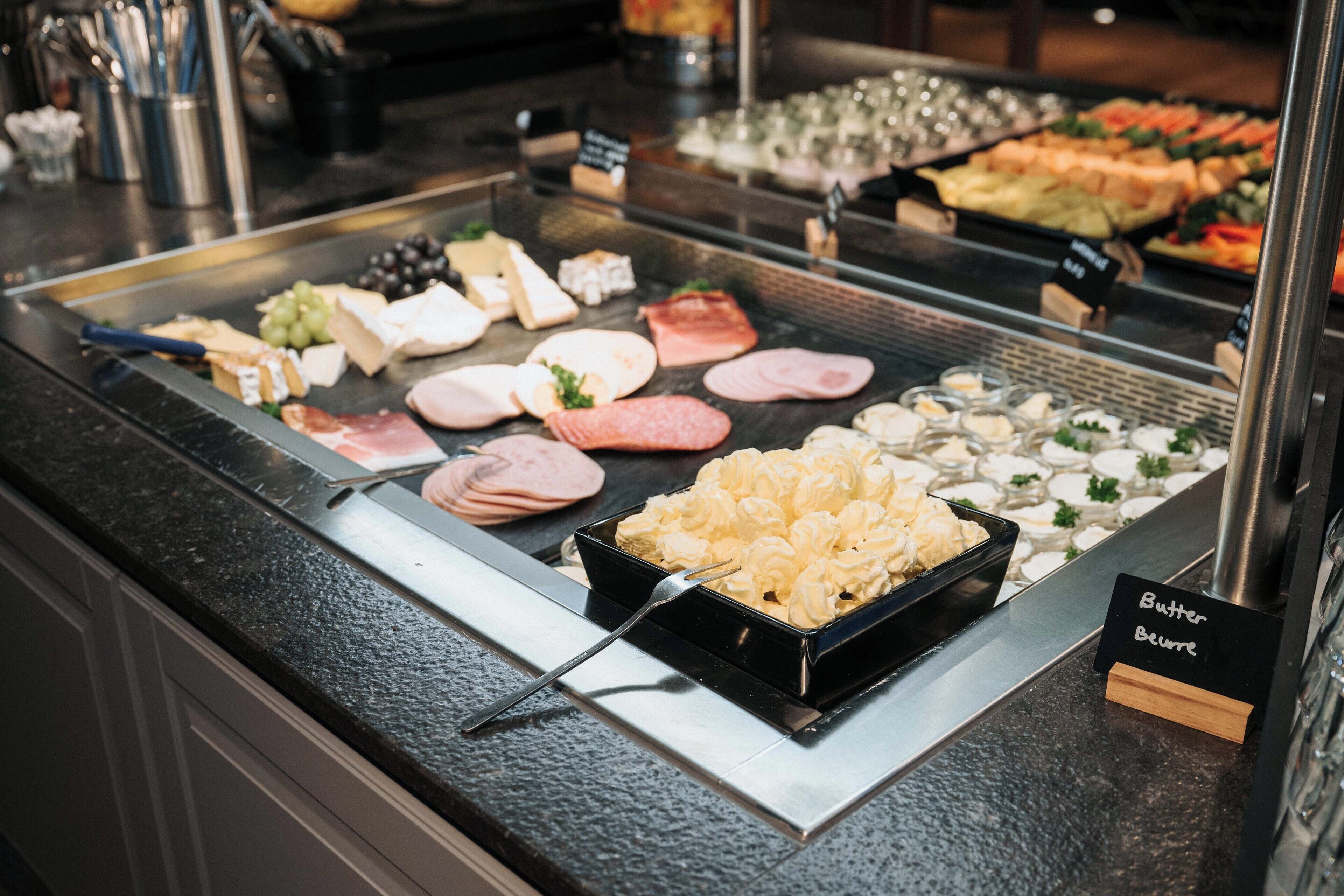A buffet with various food items including meats, cheeses, and a bowl of butter.